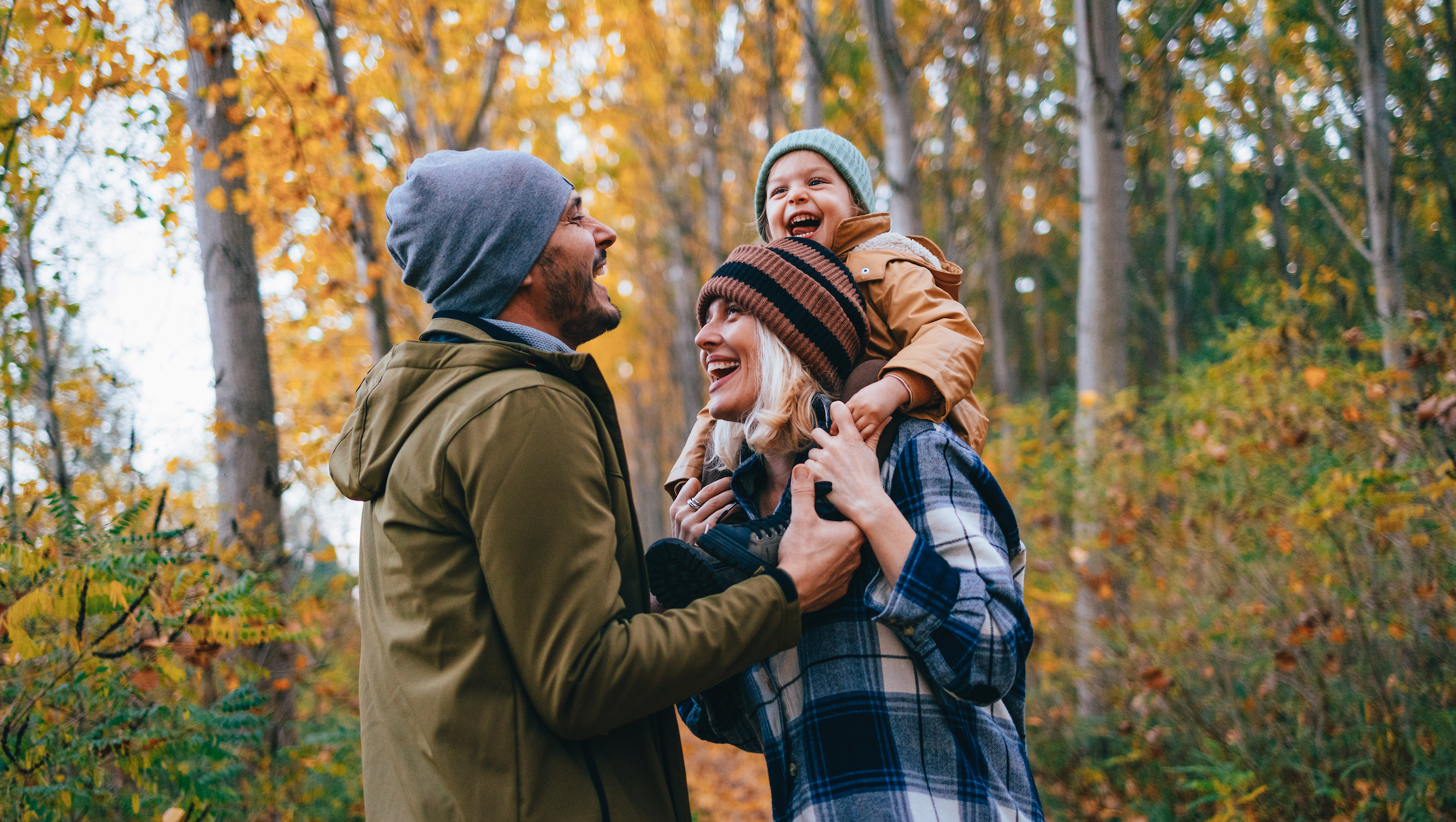 A family takes a walk in the fall woods with daughter on shoulders